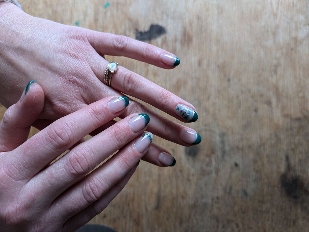 Wide shot of green French manicure with nail art resting on a warm wood table at T Nails & Spa, Seattle
